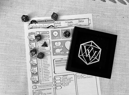 black and white image of a dungeons and dragons character sheet with a dice tray and set of polyhedral dice