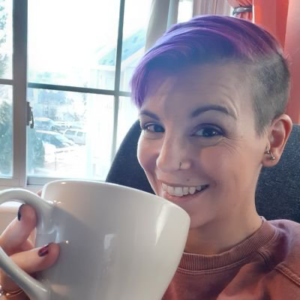 Smiling woman with purple hair and an undercut looks at the camera while drink coffee 