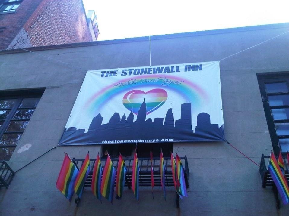 Banner Reading The Stonewall Inn hangs on a building with many pride flags