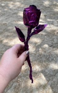 A hand holds a purple rose made from tin foil 