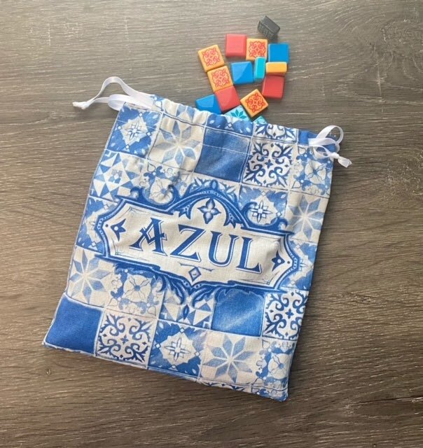 Pictured: A blue and white checkerboard Azul linen bag with multi-colored tile pieces spilling out of it.