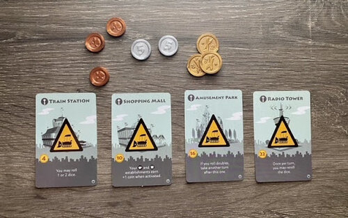 Pictured: The four grey special buildings: Train Station, Shopping Mall, Amusement Park, and Radio Tower. Also featured are the single copper, silver five, and gold ten piece coins.