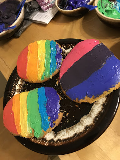 Three cookies; two frosted in red, orange, yellow, green, blue, and purple, and the last frosted in pink, purple, and blue, symbolizing the rainbow and bisexual flag, respectively.