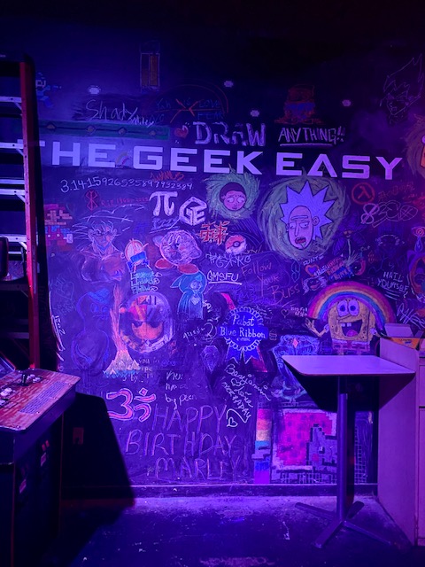 Pictured: Chalkboard reads The Geek Easy with many cartoon drawings surrounding the words