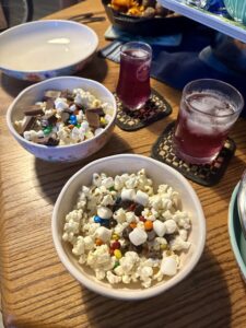 2 bowls of popcorn and candy are shown in front of 2 purple drinks